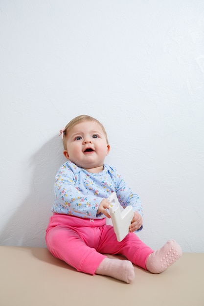 Een klein meisje, acht maanden oud, zit op de bank met een oorpiercing apparaat. Schoonheid voor jonge kinderen