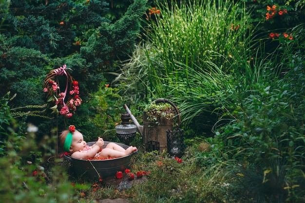 Een klein meisje baadt in een bassin met aardbeien in de tuin.