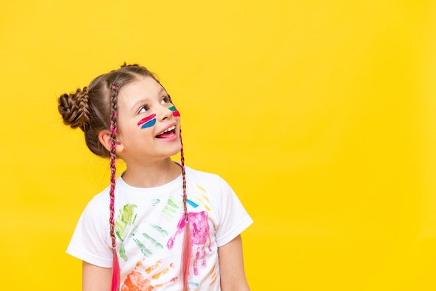 Een klein meisje beschilderd met verf kijkt naar uw advertentie op een gele geïsoleerde achtergrond De kunst van het schilderen met verf voor kinderen Kunstcursussen voor schoolkinderen Ruimte kopiëren