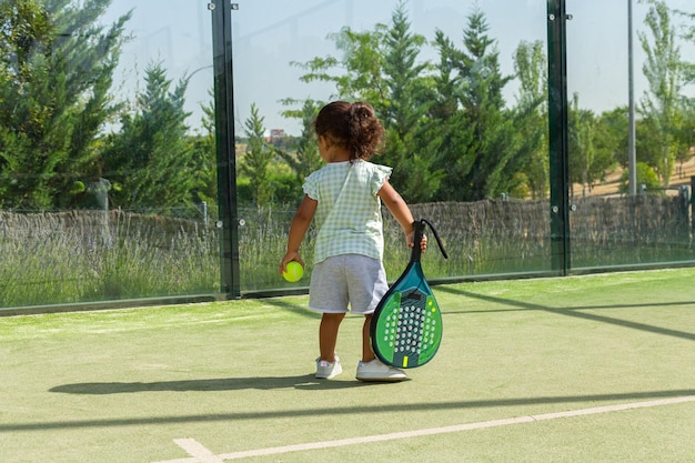 Foto een klein meisje dat een tennisbal van de grond oppakt op een paddlebaan