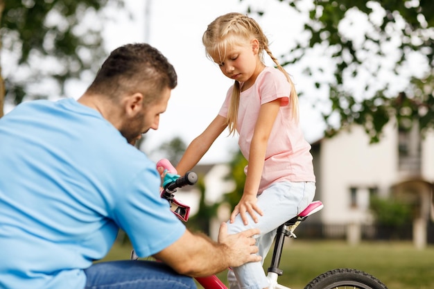 Een klein meisje dat op een fiets zat en pijn in haar been voelde, viel terwijl ze op de fiets reed in het park.
