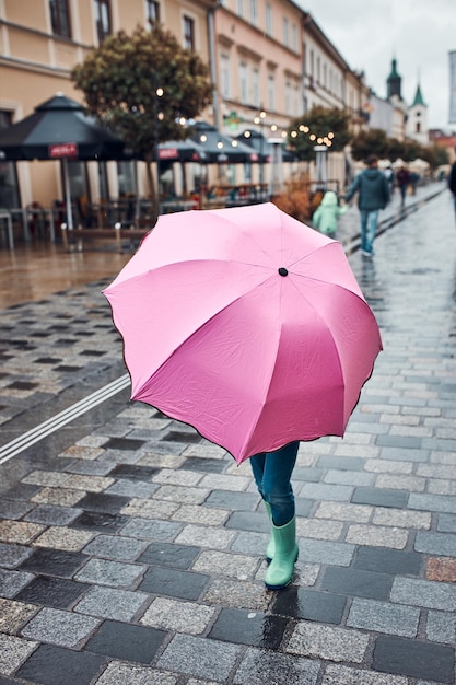 Een klein meisje dat zich verbergt achter een grote roze paraplu loopt in een centrum op een regenachtige sombere herfstdag