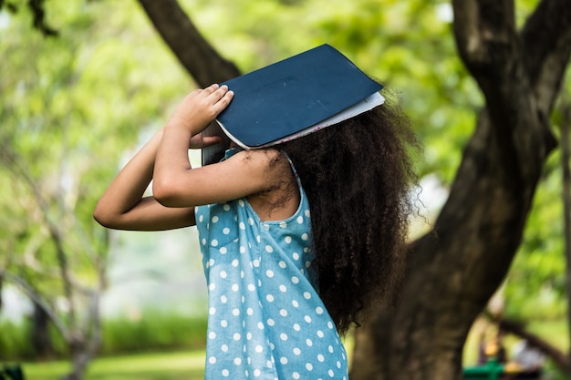 Een klein meisje die betrekking hebben op gezicht met een boek in een park