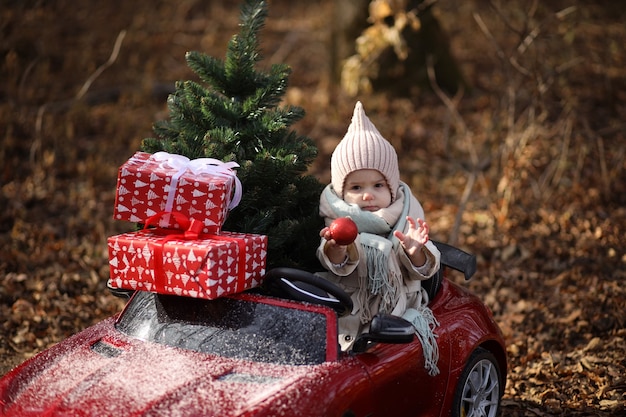 een klein meisje draagt een kerstboom en cadeautjes in een rode auto