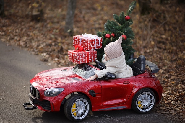 een klein meisje draagt een kerstboom en cadeautjes in een rode auto