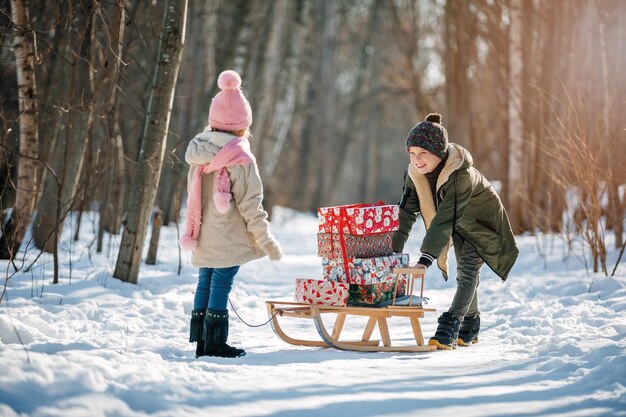 Een klein meisje en een jongen dragen de slee met kerstcadeautjes op winterse achtergrond