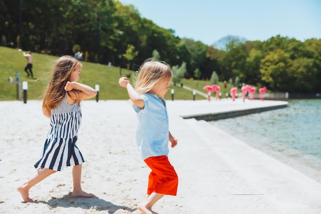 Een klein meisje en haar jongere broer spelen op het strand en gooien stenen in de waterkinderen aan de oever van het meer