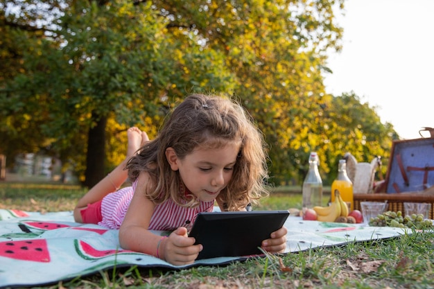 Een klein meisje gebruikt een tablet tijdens een picknick in een park kinderen en onderwijs met technologie