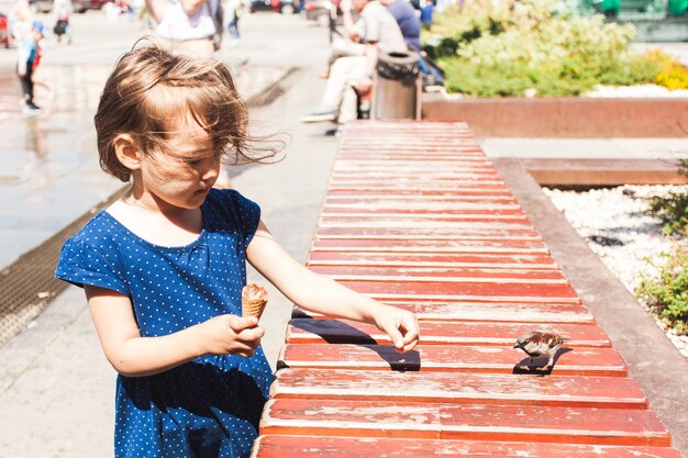 Een klein meisje geeft brood aan de vogel, mus, dieren en kinderen, ijs, stad en zomer