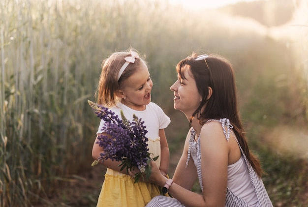 Een klein meisje geeft in de zomer een boeket lupine aan haar moeder op het veld. Concept van liefde en gelukkig gezin