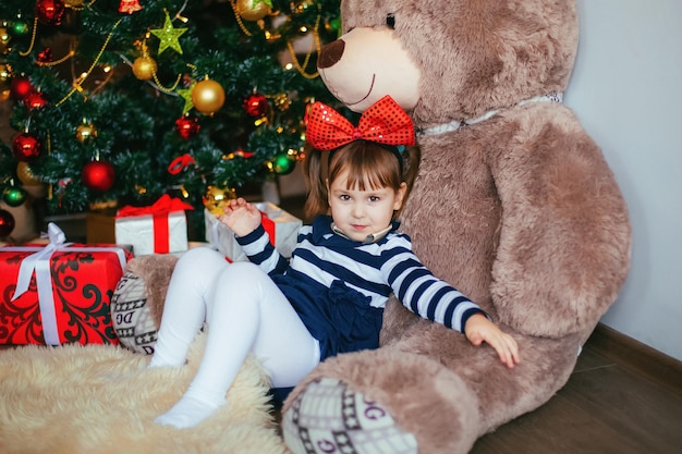 Een klein meisje geniet ervan om op een teddybeer te liggen die door de kerstman is gegeven voor het kerst- en nieuwjaarsdecor