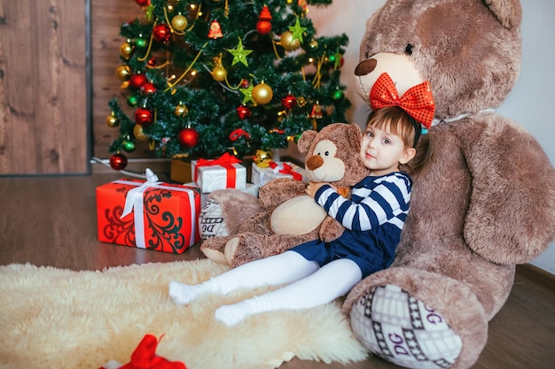 Een klein meisje geniet ervan om op een teddybeer te liggen die door de kerstman is gegeven voor het kerst- en nieuwjaarsdecor