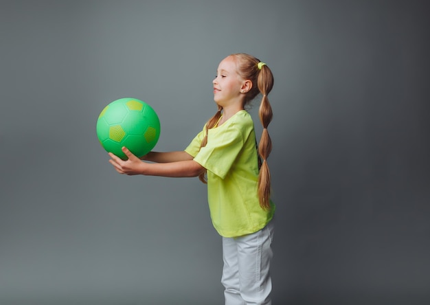 Een klein meisje gooit een bal omhoog geïsoleerd op een grijze achtergrond een kleine atleet kindersport