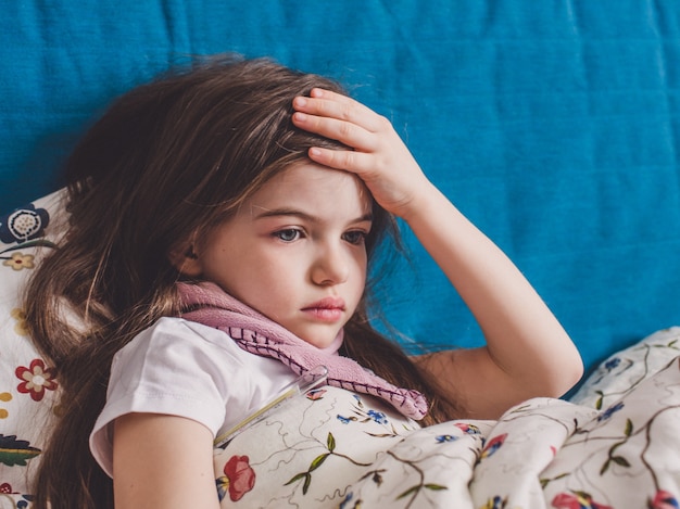 Een klein meisje heeft griep en ligt thuis onder een deken
