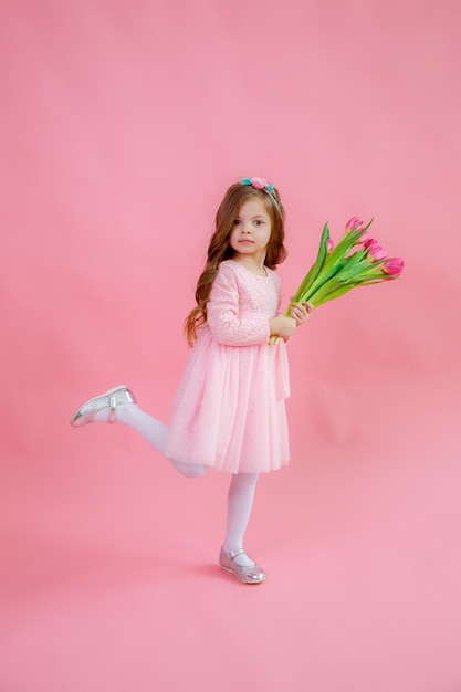 Een klein meisje houdt een boeket roze tulpen op een roze achtergrond