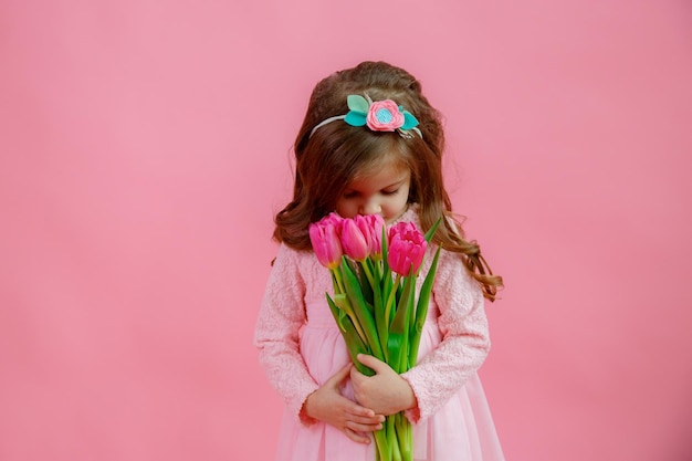 Een klein meisje houdt een boeket roze tulpen vast op een roze achtergrond