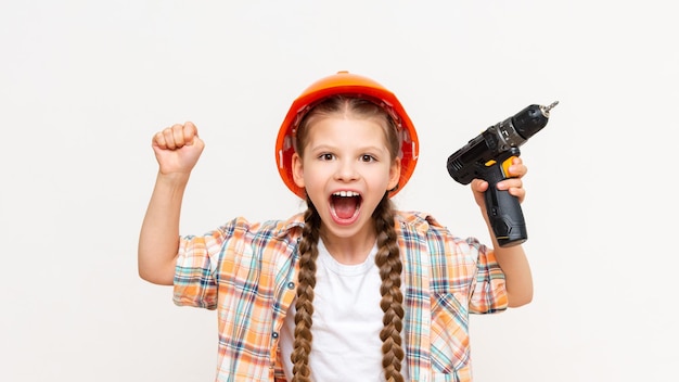 Een klein meisje houdt een boor vast en schreeuwt Een kind in een bouwhelm op een witte geïsoleerde achtergrond Het concept van renovatie in de kinderkamer