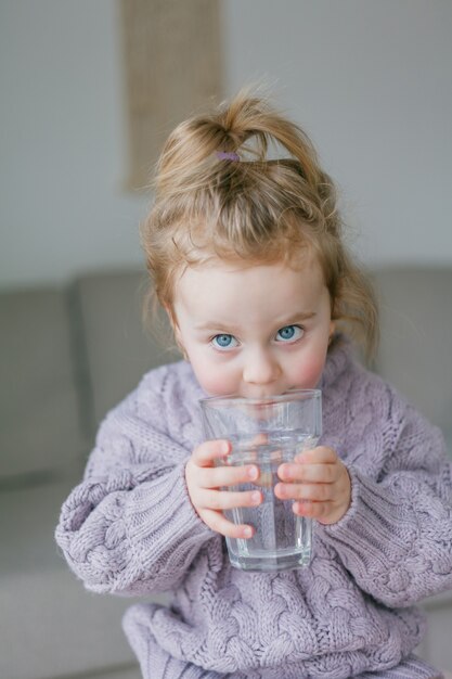 Een klein meisje houdt een glas water vast, drinkt. knus.