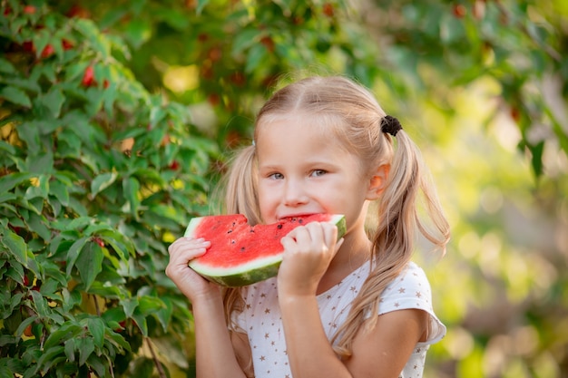 Een klein meisje houdt een stuk watermeloen vast in de zomerzon