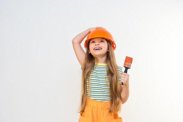 Een klein meisje houdt met haar hand een bouwhelm op haar hoofd en met haar andere hand een kwast voor het schilderen van muren in een kinderkamer.