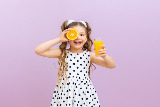 Een klein meisje houdt sinaasappelsap en een sinaasappel vast Een kind in een jurk met stippen drinkt vers geperst sap