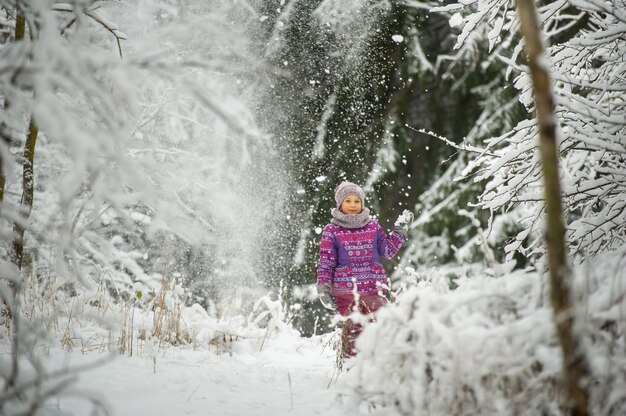 Een klein meisje in de winter in paarse kleren loopt door een besneeuwd bos