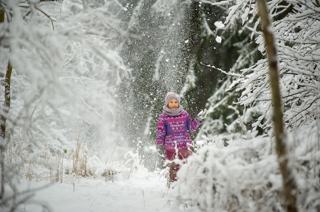Een klein meisje in de winter in paarse kleren loopt door een besneeuwd bos
