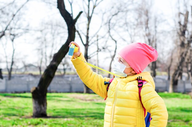 Een klein meisje in een beschermend masker tijdens de quarantaine loopt buiten in het voorjaar en maakt een selfie op een kindercamera.