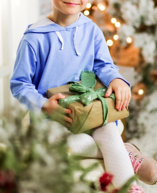 Een klein meisje in een blauwe hoodie zit en nieuwjaarsdecor op een bankje met een cadeau in haar handen. Foto