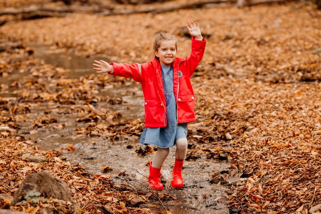 Een klein meisje in een jas en rode rubberen laarzen wandelen in het herfstbos. Hoge kwaliteit foto