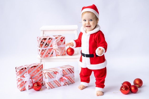 Een klein meisje in een kerstmankostuum staat met kerstcadeaus in dozen op een witte achtergrond newyea