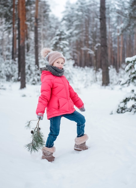 Een klein meisje in een lichte jas speelt in het besneeuwde winterbos.