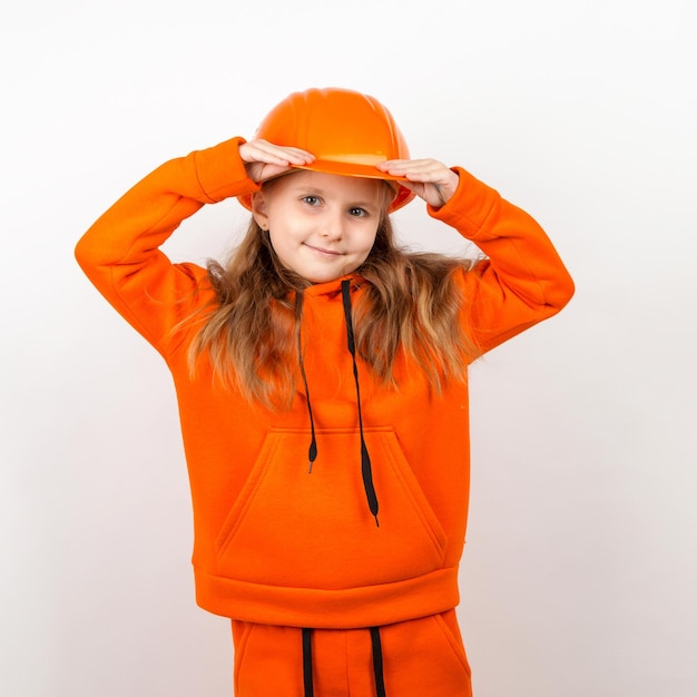 Een klein meisje in een oranje pak en een bouwhelm een concept van jonge bouwer portret witte achtergrond dag van de arbeid