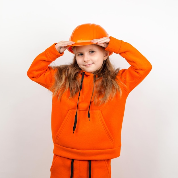 Een klein meisje in een oranje pak en een bouwhelm een concept van jonge bouwer Portret witte achtergrond Dag van de Arbeid