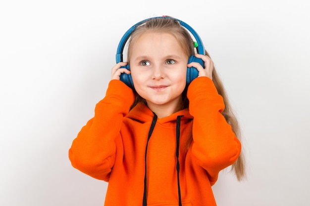 Een klein meisje in een oranje pak luisteren naar muziek in blauwe koptelefoon op witte achtergrond