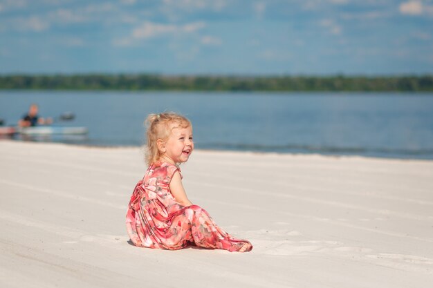 Een klein meisje in een prachtige sarafna speelt in het zand op het strand.