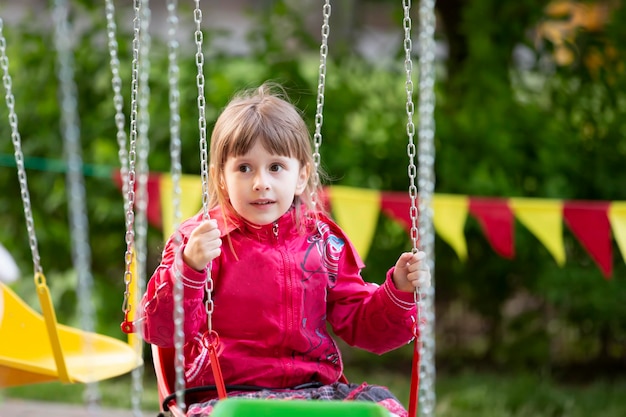 Een klein meisje in een rood jasje zit op een kettingcarrouselrit