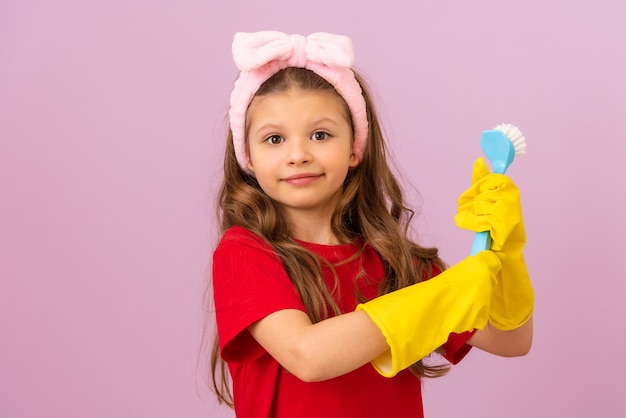 Een klein meisje in een rood T-shirt en rubberen handschoenen houdt een schoonmaakborstel vast.