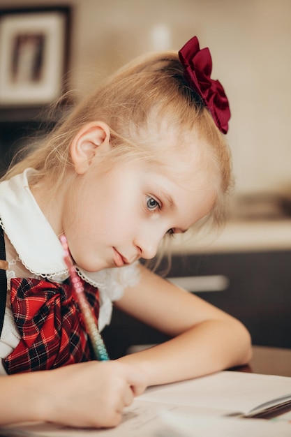 Een klein meisje in een schooluniform maakt thuis huiswerk in een werkboek