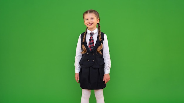 Een klein meisje in een schooluniform op een groene achtergrond kopie ruimte