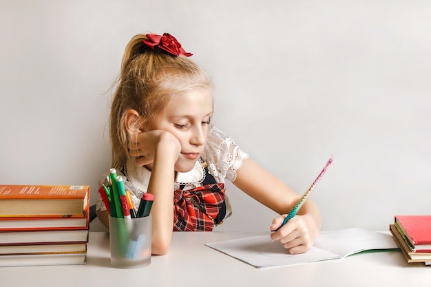 Een klein meisje in een schooluniform tekent met haar linkerhand in een notitieboekje