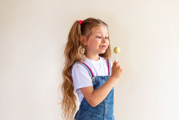 Een klein meisje in een spijkerrok houdt een lolly vast