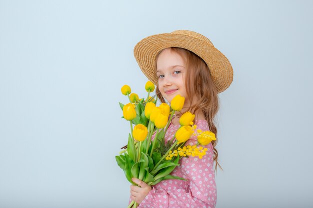 Een klein meisje in een strohoed houdt een boeket gele tulpen vast die op een witte achtergrond worden geïsoleerd