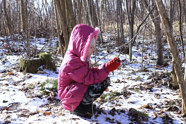 Een klein meisje in een warme jas wandelt door het winterbos en verkent de natuur