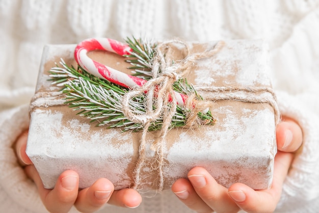 Een klein meisje in een witte trui heeft een kerstcadeau in haar handen.