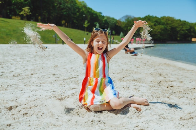 Een klein meisje in een zomerjurk gooit zand op het strand zomervakantie