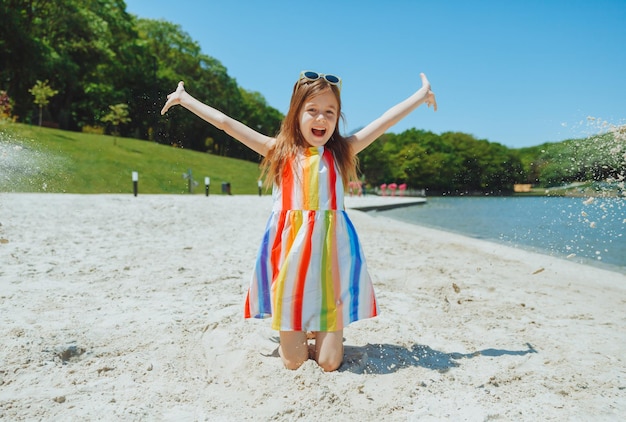 Een klein meisje in een zomerjurk gooit zand op het strand zomervakantie