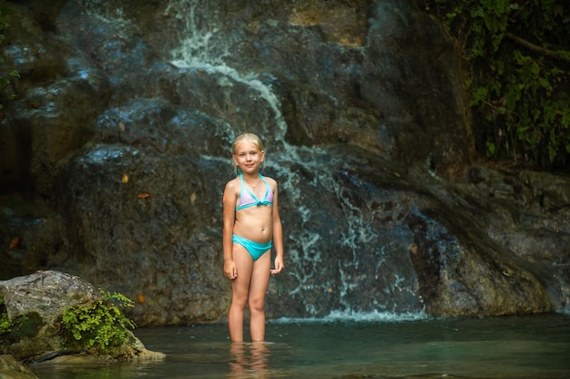 Een klein meisje in een zwembroek bij een waterval in de jungle. natuurreis in de buurt van een prachtige waterval, turkije.