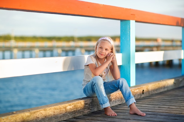 Een klein meisje in jeans en een T-shirt zit op een pier in de buurt van de Baltische Zee. Palanga, Litouwen