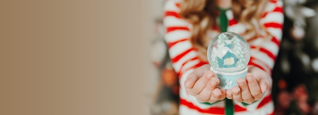 Een klein meisje in pyjama en een kerstmuts houdt een kerstbal vast een sneeuwbol Kerstmis